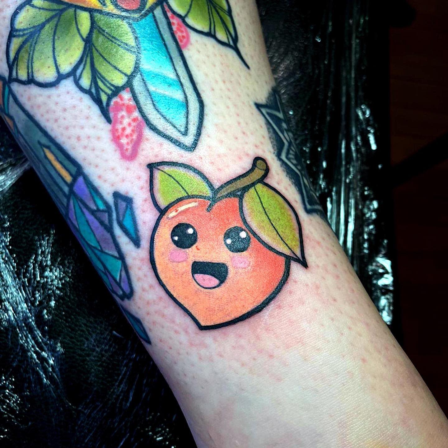 A tattoo of a cute, smiling peach with a leaf on an arm